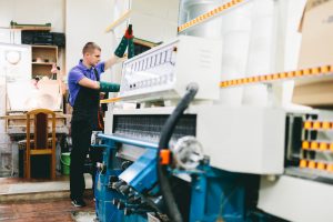 Glazier worker operates glass cutting machine in workshop