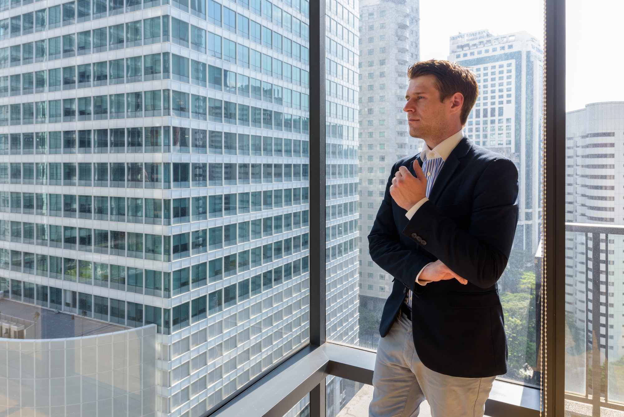 Young handsome businessman standing against glass window in city